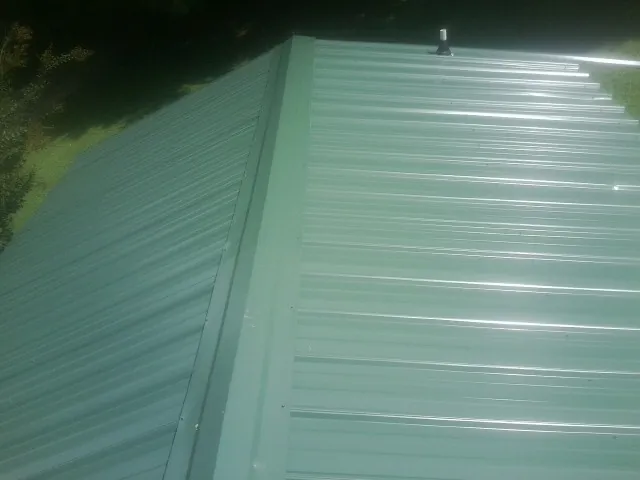 New green metal panels meeting at the ridge of a roof — Flat Roof Repair work by our crew in Plano
