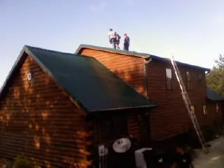 Crew on the ridge of a green metal roof on a two story log home in Plano