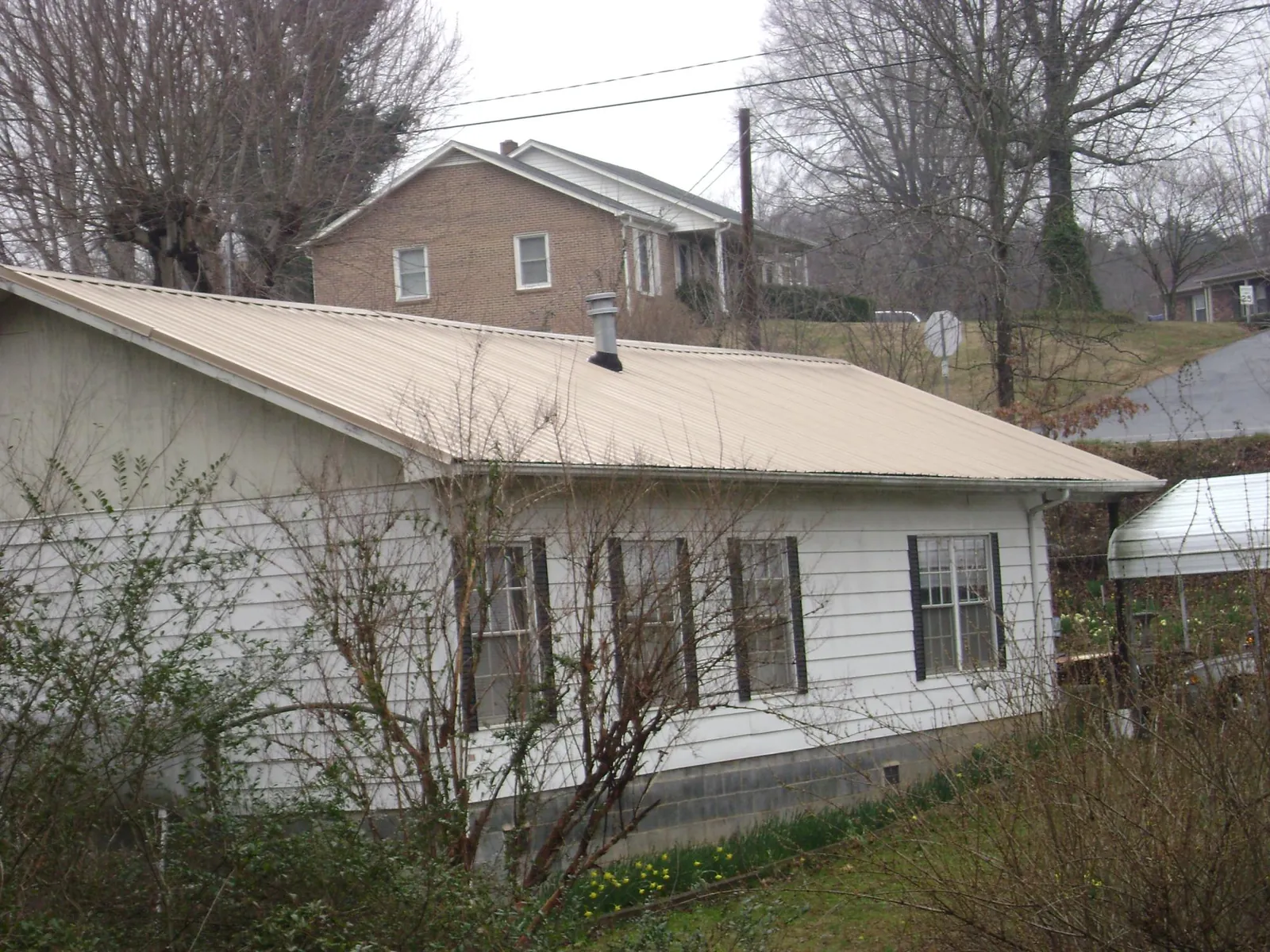 Tan metal roof on a white sided house set into a hillside — Commercial Roofing by Roofing Brothers in Plano